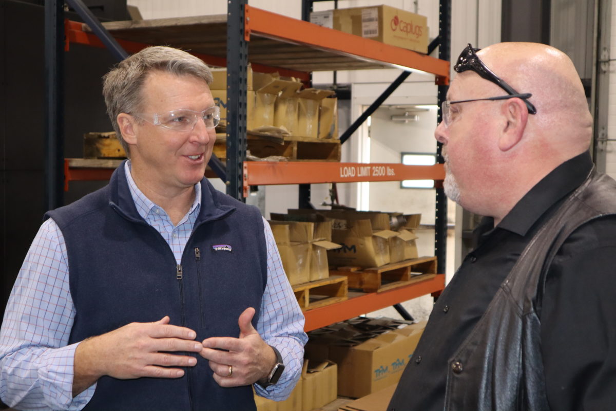 2 men speaking to each other inside of a warehouse building.