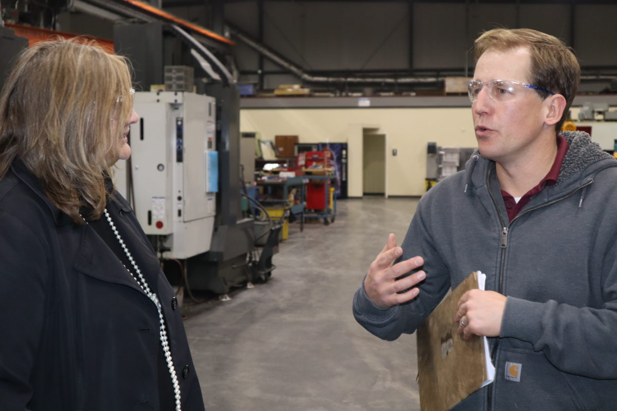 A woman on the left looking at a man on the right who is speaking, inside of a warehouse type building.