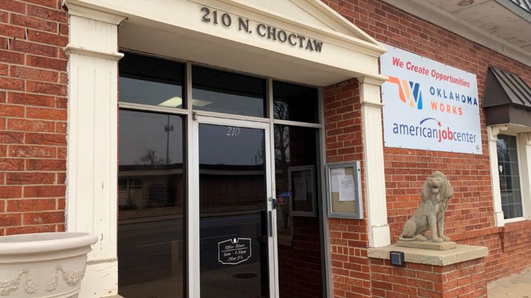 Red brick with beige wood frame around front glass door. 210 N. Choctaw above the door. Stone statue of a lion to the right of the door. Sign to the right of the door on the exterior wall stating "We Create Opportunities" with Oklahoma Works Logo.