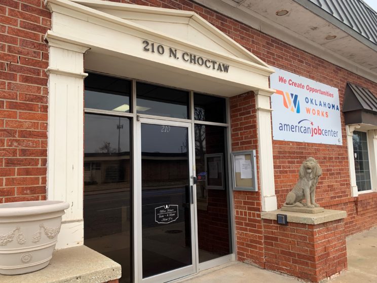 Red brick with beige wood frame around front glass door. 210 N. Choctaw above the door. Stone statue of a lion to the right of the door. Sign to the right of the door on the exterior wall stating "We Create Opportunities" with Oklahoma Works Logo.