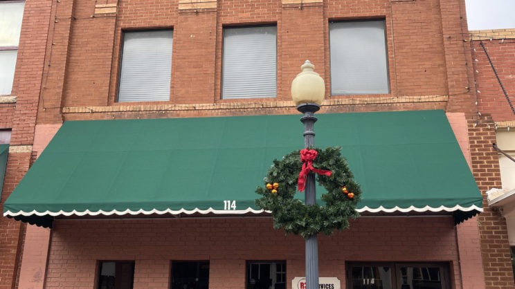 Red brick building with green fabric awning with 114 on the awning. Light post on the sidewalk outside the building.