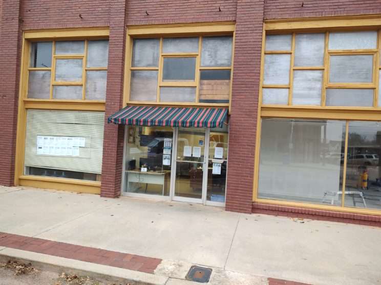 Red-brown brick exterior. A striped fabric awning over the glass front door.